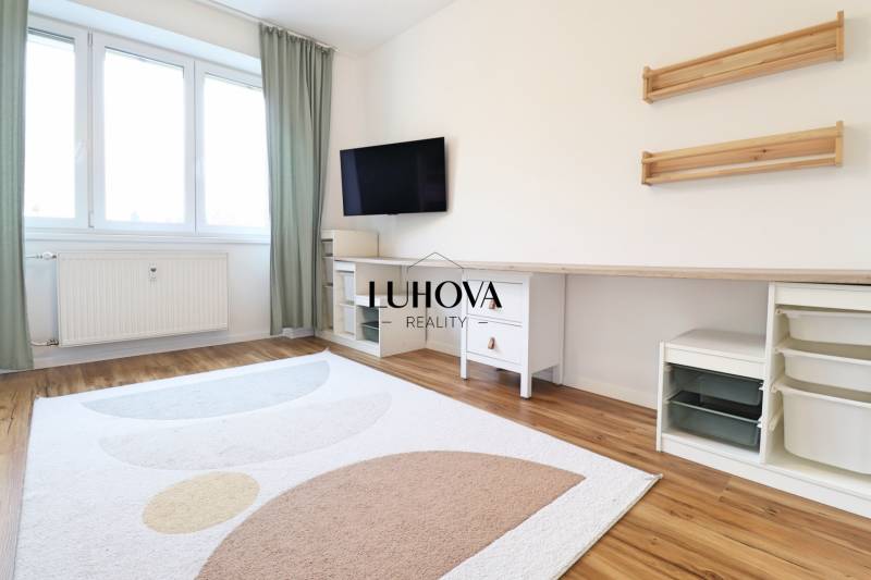 Pokoj v 3-pokojovém bytě s televizí, bílým nábytkem a podlahou s dřevěným dekorem.