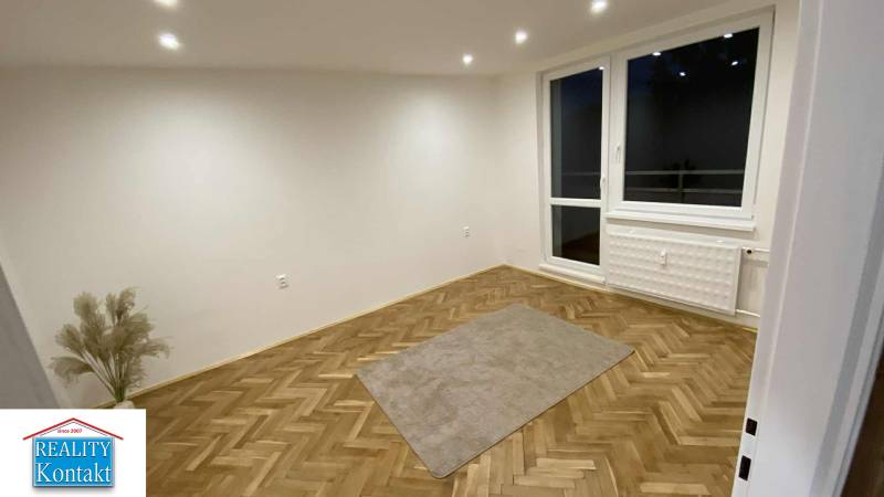 Pokoj v 1-pokojovém bytě s podlahou s dřevěným dekorem a velkým oknem.