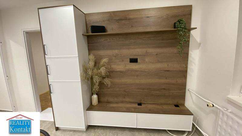 V 1-pokojovém bytě je šatníková stěna s dřevěným dekorem a květinami ve váze.