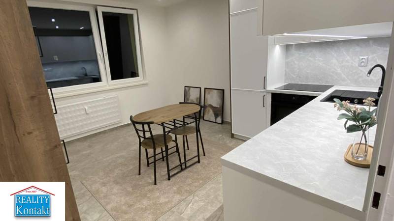 Kuchyně v 1-pokojovém bytě s jídelním stolem, skříněmi a dekoračními obrazy na stěně.