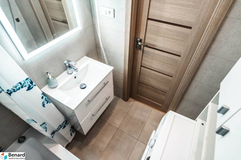 Koupelna v 2-pokojovém bytě s umyvadlem, zrcadlem a dřevěnými dveřmi.