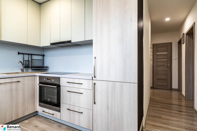 Kuchyně v 2pokojovém bytě s podlahou s dřevěným dekorem a světlými skříňkami.