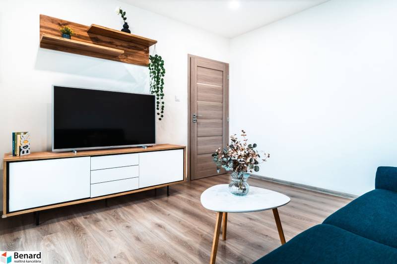 Obývací pokoj s televizí, skříní, stoličkou a podlahou s dřevěným dekorem v 2-pokojovém bytě.