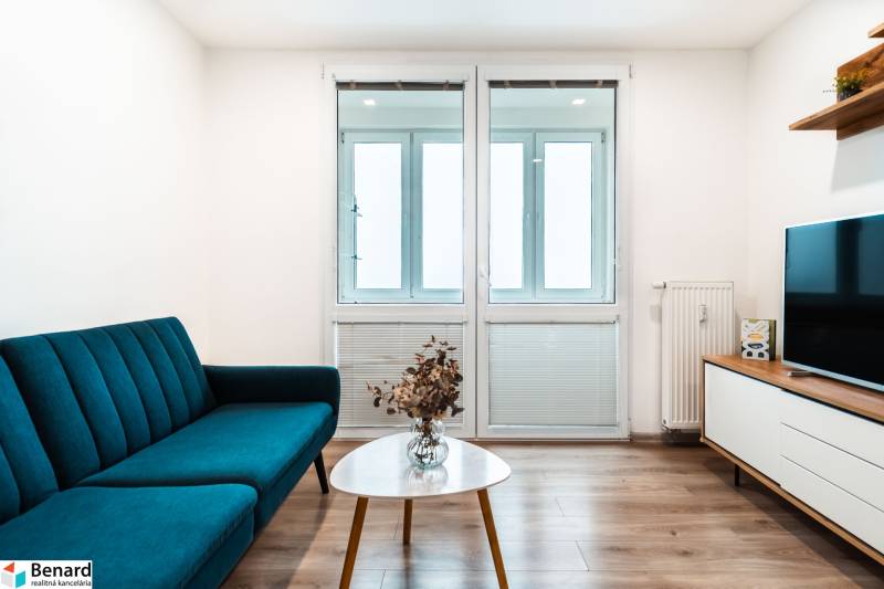 Obývací pokoj v 2-pokojovém bytě s pohovkou, televizorem a podlahou s dřevěným dekorem.