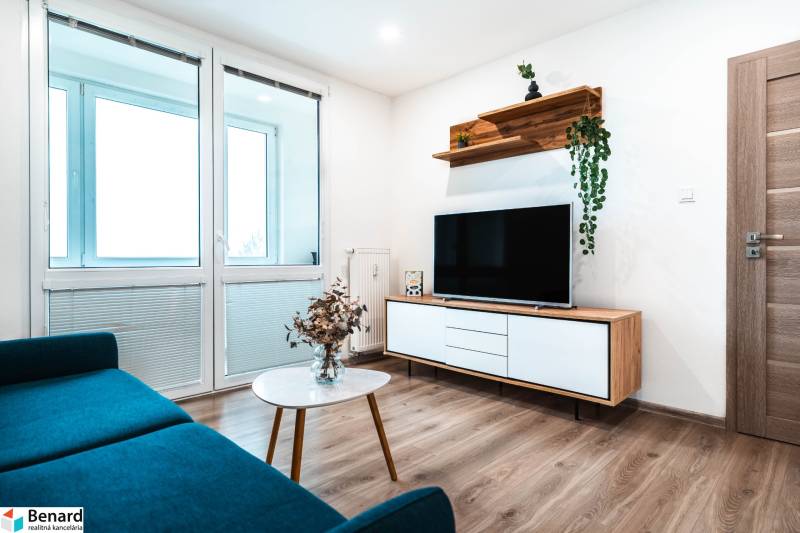 Obývací pokoj v 2-pokojovém bytě s pohovkou, televizí a podlahou s dřevěným dekorem.