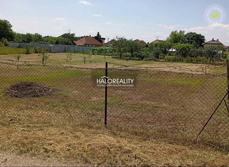 Zahrady v Marcelové s travnatým povrchem a oplocením, stromy v pozadí.