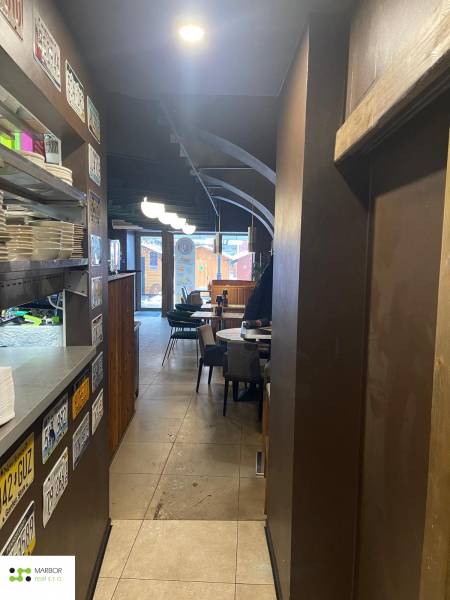 Interiér gastro prostorů s talíři na polici, tabule, stoly a židle.