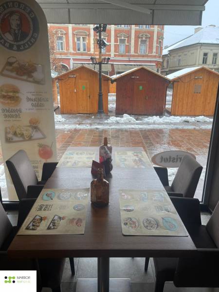 Zimní scenérie přes okno gastro prostoru s pohledem na dřevěné stolky.