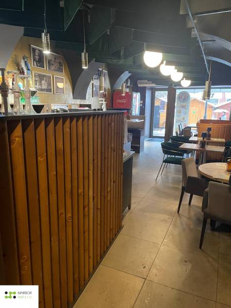 Interiér gastro prostorů s dřevěným barem a stoly. Vidět je i dekorativní osvětlení.