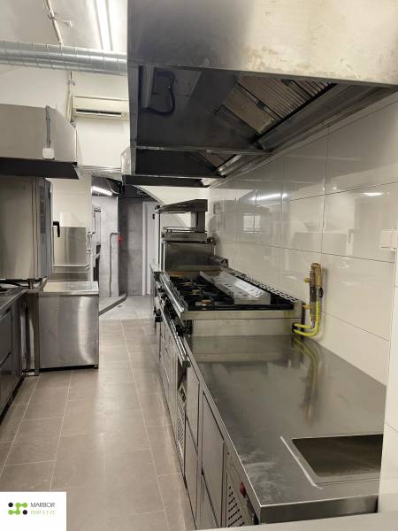 Profesionální kuchyně s nerezovými spotřebiči a bílými kachličkami v gastro prostorech.