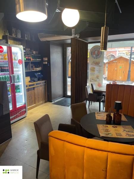 Interiér gastro prostor s kruhovým stolem, židlemi a osvětlením.