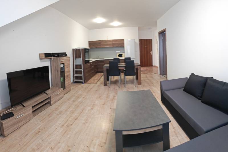 Obývací pokoj v 3-pokojovém bytě s podlahou s dřevěným dekorem, kuchyňským koutem a pohovkou.