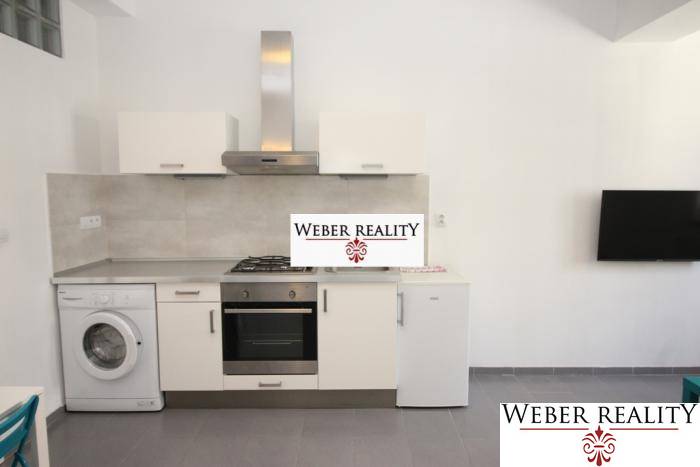 Kuchyně v 2-pokojovém bytě se spotřebiči a televizorem na stěně.