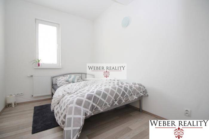 Ložnice v dvoupokojovém bytě s postelí a podlahou s dřevěným dekorem.