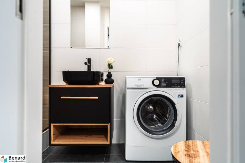 Koupelna v 2-pokojovém bytě s umyvadlem, pračkou a černými doplňky.