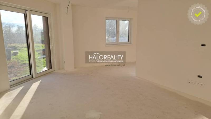 Interiér rodinného domu s velkým oknem, bílými stěnami a terasovými dveřmi.