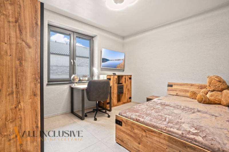 Dětský pokoj v rodinném domě s pracovním stolem, postelí a podlahou s dřevěným dekorem.