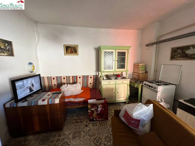 Pokoj s gaučem, kuchyňskou linkou, sporákem a televizí v rodinném domě.