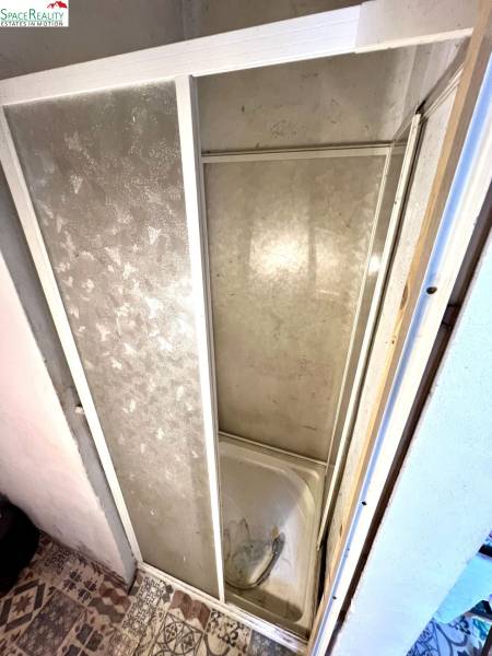 Sprchový kout v interiéru rodinného domu s obkladem a dekorativní podlahou.