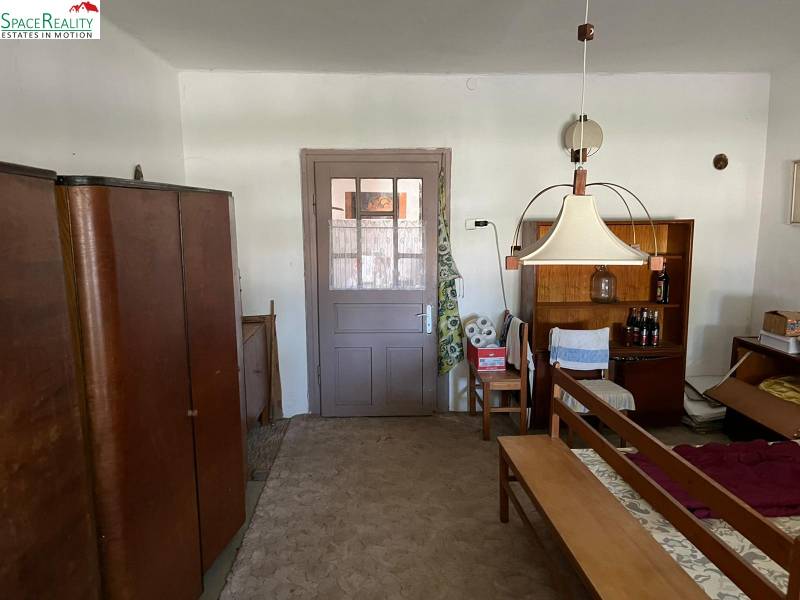 Interiér rodinného domu s nábytkem a kobercem, středová lampa a police s nápoji.