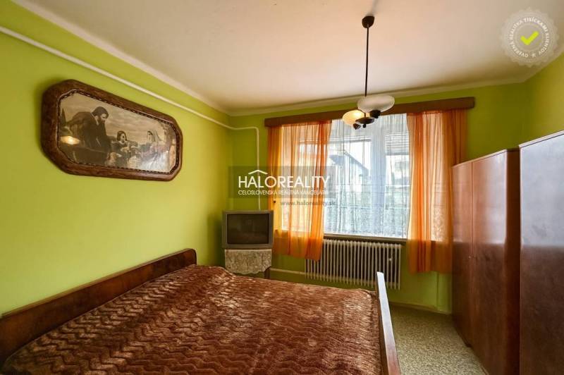 Ložnice v rodinném domě s postelí, obrazem, skříňkou a televizí.