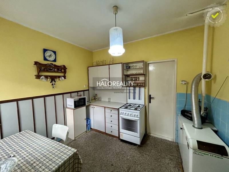 Kuchyně v rodinném domě se žlutými stěnami, bílým nábytkem a kobercovým povrchem.