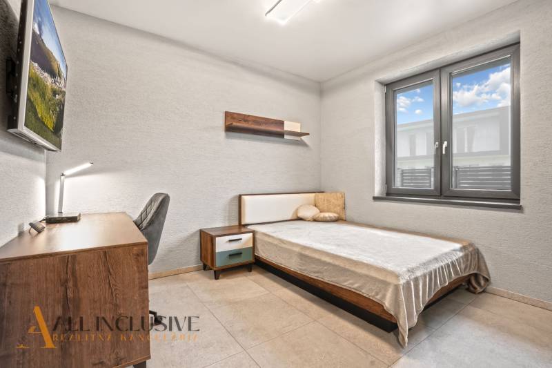 Ložnice v rodinném domě s jednoduchým zařízením, psacím stolem a pohodlnou postelí.