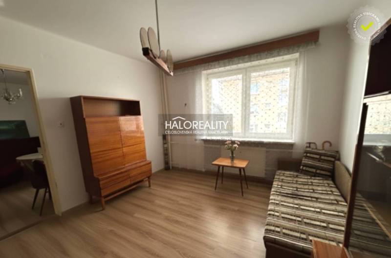 Obývací pokoj v 3-pokojovém bytě s podlahou s dřevěným dekorem, sedačkou, skříňkou a oknem.