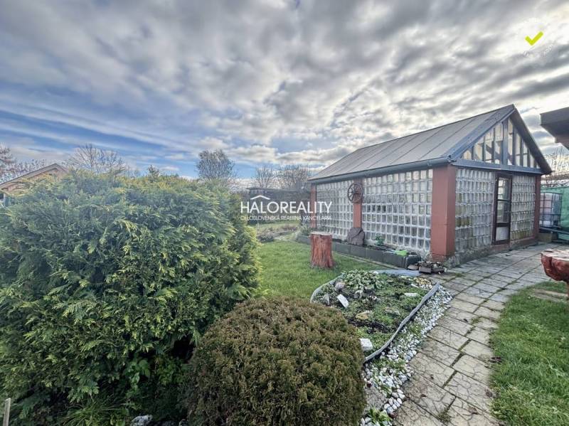 Zahrady ve Spišské Nové Vsi se skleněným domem, upraveným trávníkem a květinovým záhonem.