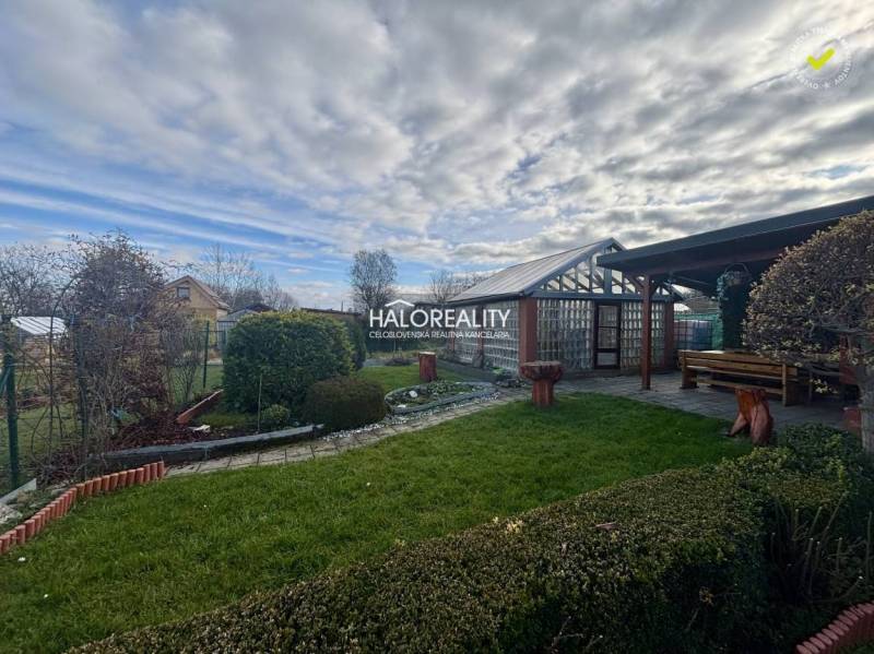 Zahrady Spišské Nové Vsi s upravenými keři, trávníkem a dřevěným přístřeškem.