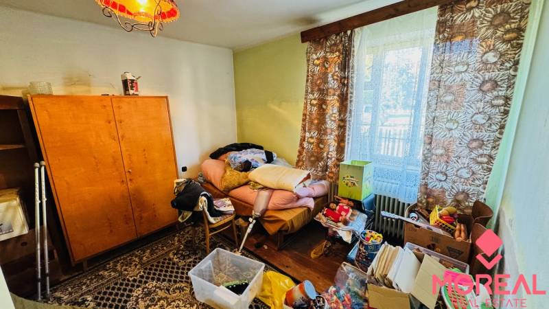 Pokoj v rodinném domě s nepořádkem, starým nábytkem a výhledem z okna.