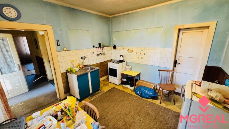 Kuchyně v rodinném domě s modrými stěnami, starším nábytkem a praktickým vybavením.