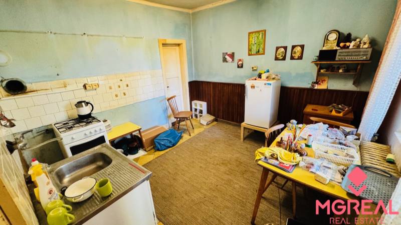 Kuchyně v rodinném domě s jídelním stolem, starším sporákem a ledničkou.