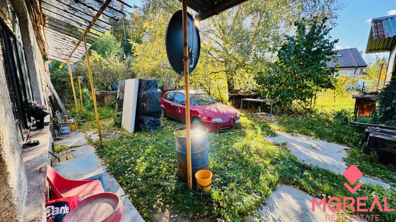 Rodinný dům v Brodzanech s červeným autem na zahradě obklopený zelení a dřevem.