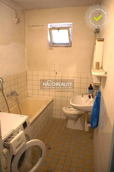 Koupelna se starší vanou, umyvadlem a pračkou v rodinném domě.