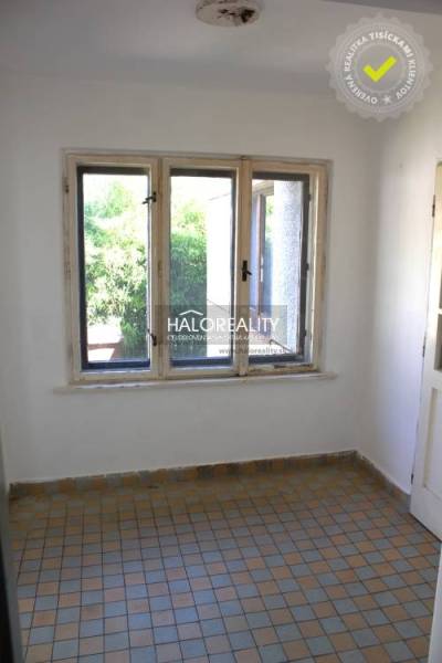 Pokoj v rodinném domě s dlaždicovou podlahou a okny směřujícími do zeleně.