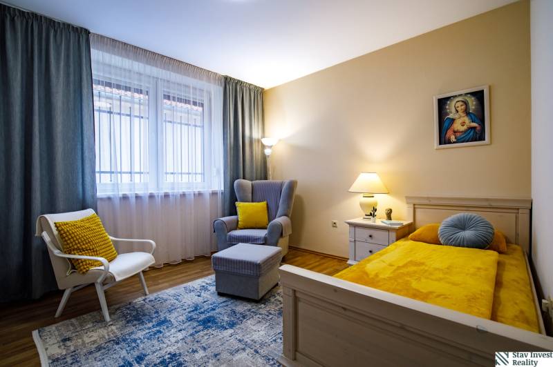 Pokoj v rodinném domě s postelí, křeslem, stolkem a podlahou s dřevěným dekorem.