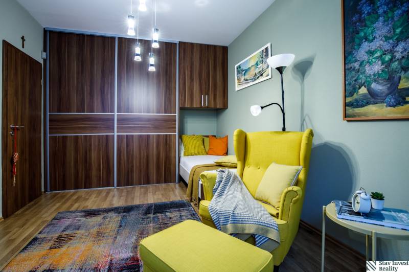 Pokoj s pohodlným křeslem, šatní skříní, lustrem a podlahou s dřevěným dekorem v rodinném domě.