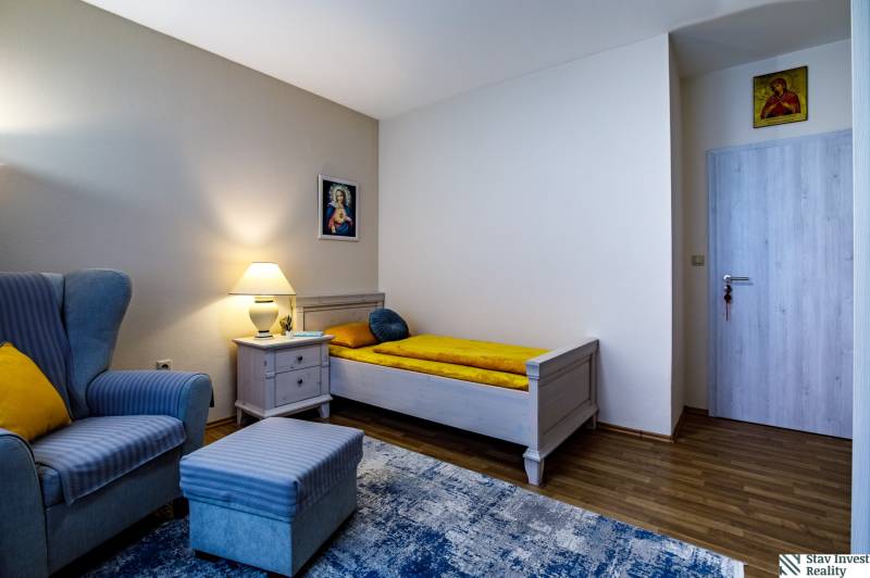 Pokoj rodinného domu s křeslem, postelí, nočním stolkem a podlahou s dřevěným dekorem.