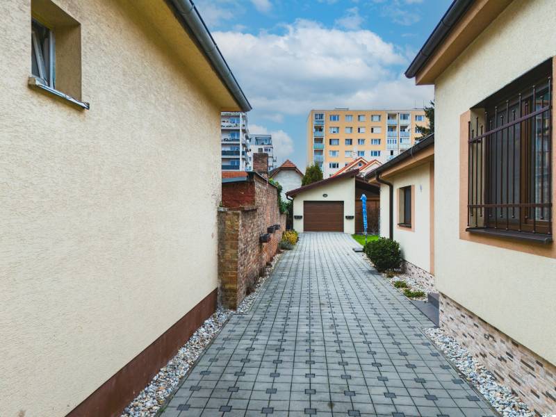 Pohled na dvůr rodinného domu z Školní ulice v Senci s chodníkem a keři.