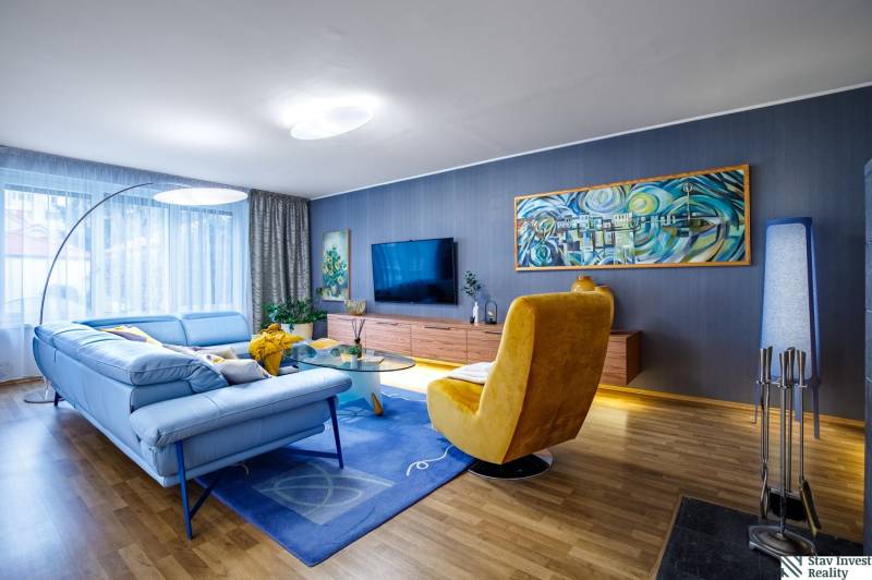 Obývací pokoj v rodinném domě s modrou sedačkou, žlutým křeslem a podlahou s dřevěným dekorem.