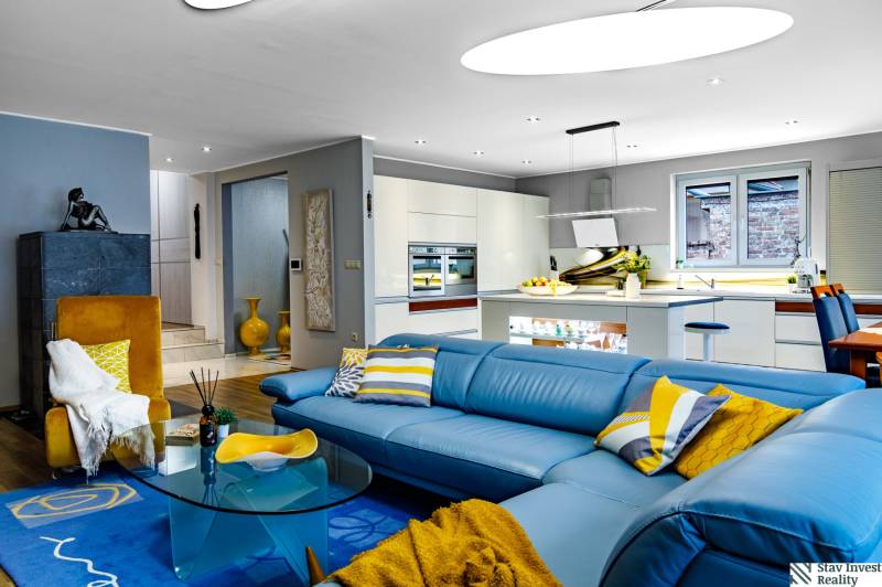 Obývací pokoj v rodinném domě s modrou sedačkou a kuchyní, podlaha s dřevěným dekorem.