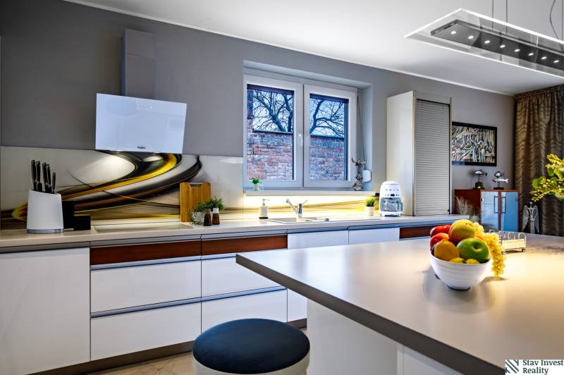 Kuchyně v rodinném domě se stylovou deskou, bílými skříňkami a dekoracemi na okně.