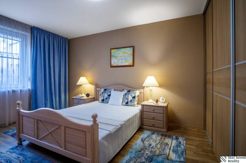 Ložnice v rodinném domě s postelí, nočními stolky a podlahou s dřevěným dekorem.