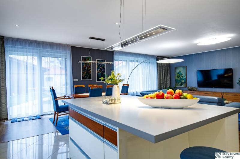 Obývací pokoj v rodinném domě s kuchyňským ostrůvkem, pohovkou a jídelním stolem.