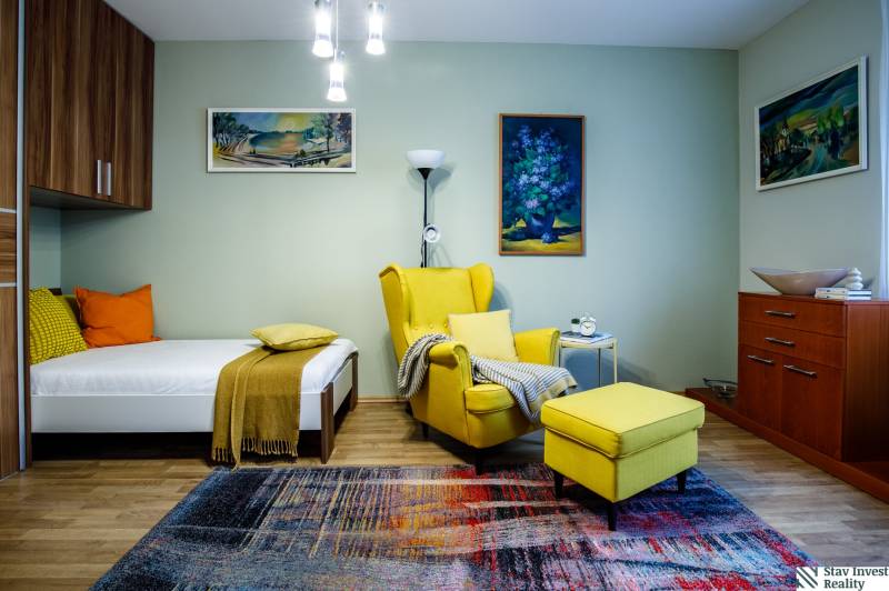 Pokoj rodinného domu s křeslem, postelí, kobercem a dekoracemi. Podlaha s dřevěným dekorem.