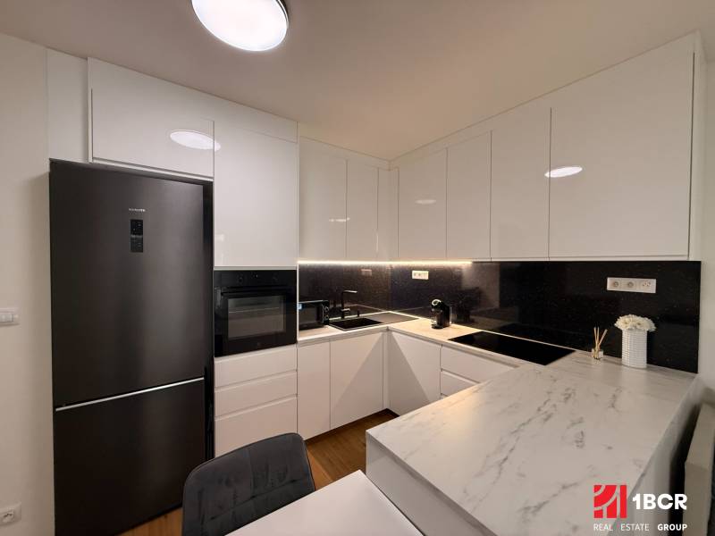 Kuchyně 2pokojového bytu s bílými skříňkami a podlahou s dřevěným dekorem.