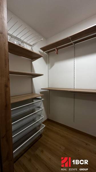 Úložné prostory s drátěnými koši a poličkami v 2-pokojovém bytě, podlaha s dřevěným dekorem.