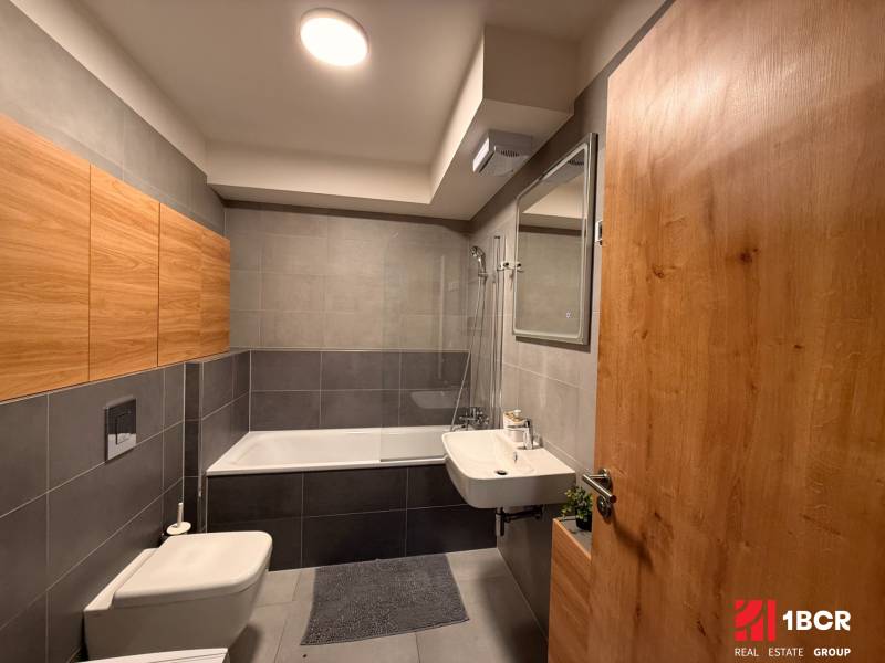 Koupelna 2pokojového bytu s dlažbou a dřevěným dekorem na úložných skříňkách.