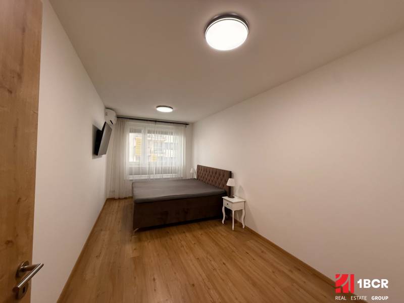 Ložnice s postelí, TV a podlahou s dřevěným dekorem v 2-pokojovém bytě.